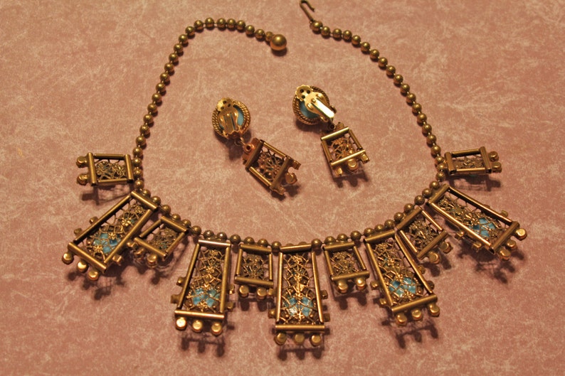Puede incluir: Un collar de oro con una cadena delicada y m&uacute;ltiples colgantes rectangulares. Cada colgante presenta un dise&ntilde;o de filigrana y una piedra azul turquesa. Tambi&eacute;n se incluyen pendientes a juego con el mismo dise&ntilde;o.