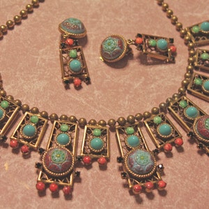 Puede incluir: Un collar de oro con detalles en turquesa y esmalte rojo. El collar presenta un dise&ntilde;o geom&eacute;trico con m&uacute;ltiples marcos rectangulares. El collar se combina con pendientes a juego.