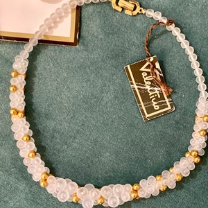 Puede incluir: Un collar de cuentas blancas y doradas con un cierre dorado. El collar est&aacute; hecho de cuentas peque&ntilde;as y redondas y tiene una etiqueta que dice "Valentino".