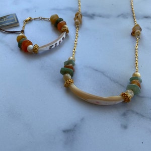 Puede incluir: Un collar y un brazalete a juego de cadena dorada con un colgante de concha y cuentas de piedras preciosas de colores.