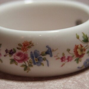 Peut inclure: Bracelet en c&eacute;ramique blanche avec un motif floral. Les fleurs sont roses, bleues, jaunes et vertes.