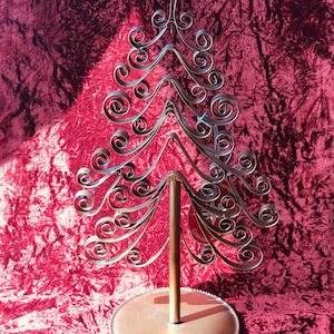 May include: A gold metal Christmas tree ornament holder with a round base and a decorative, swirling design. The holder is on a red velvet surface.