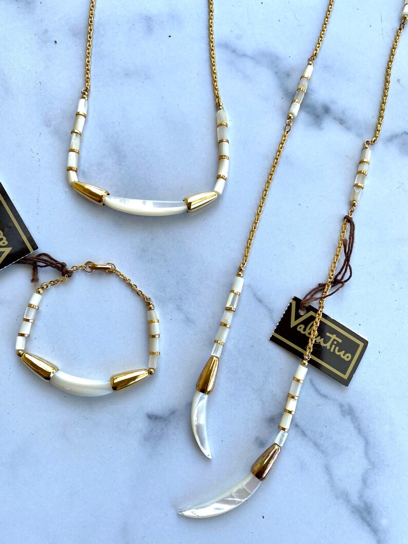 Puede incluir: Un conjunto de tres collares de oro con detalles de concha blanca. Los collares presentan una forma de media luna y est&aacute;n hechos con peque&ntilde;as cuentas redondas. Los collares est&aacute;n etiquetados como "Valentino".