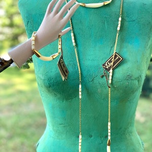 Puede incluir: Un conjunto de tres collares de cadena dorada con cuentas blancas de hueso y colgantes. Los collares se muestran en un maniqu&iacute; verde. La etiqueta en el collar dice "Valentino."