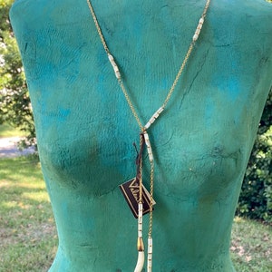 Puede incluir: Un collar de cadena dorada con cuentas de concha blanca y tres colgantes de concha blanca. El collar est&aacute; en un maniqu&iacute; con un torso verde azulado.