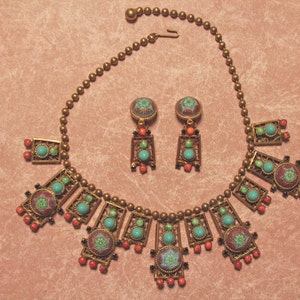 Puede incluir: Un collar y pendientes de oro con detalles en turquesa, coral y esmalte verde. El collar presenta un dise&ntilde;o geom&eacute;trico con m&uacute;ltiples colgantes rectangulares.