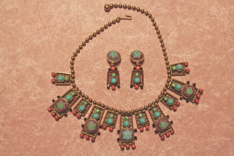Puede incluir: Un collar y pendientes de oro con detalles en turquesa, coral y esmalte verde. El collar presenta un dise&ntilde;o geom&eacute;trico con m&uacute;ltiples colgantes rectangulares.