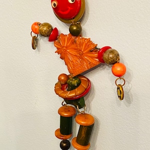 May include: A vintage button brooch featuring a smiling face with a red button, a carved flower, and a variety of colorful and patterned buttons. The brooch is made of plastic and metal.