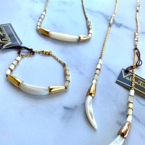 Puede incluir: Un conjunto de tres collares de oro y blanco con colgantes en forma de media luna. Los collares est&aacute;n hechos de peque&ntilde;as cuentas doradas y piezas de concha blanca.