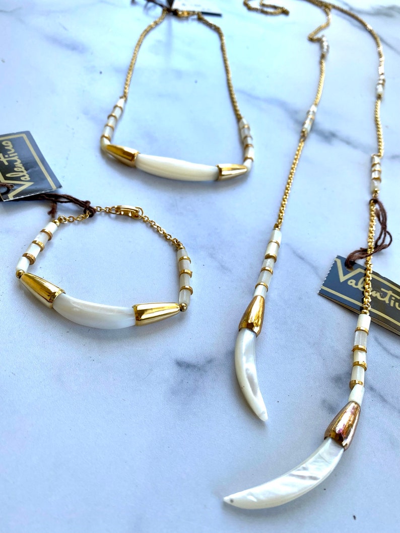 Puede incluir: Un conjunto de tres collares de oro y blanco con colgantes en forma de media luna. Los collares est&aacute;n hechos de peque&ntilde;as cuentas doradas y piezas de concha blanca.