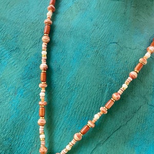 May include: A long necklace made of brown, white, and pink beads with a gold pendant at the bottom.