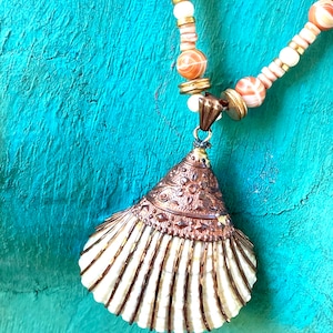 May include: A white seashell pendant necklace with a copper-toned top and a beaded chain with white and orange beads.