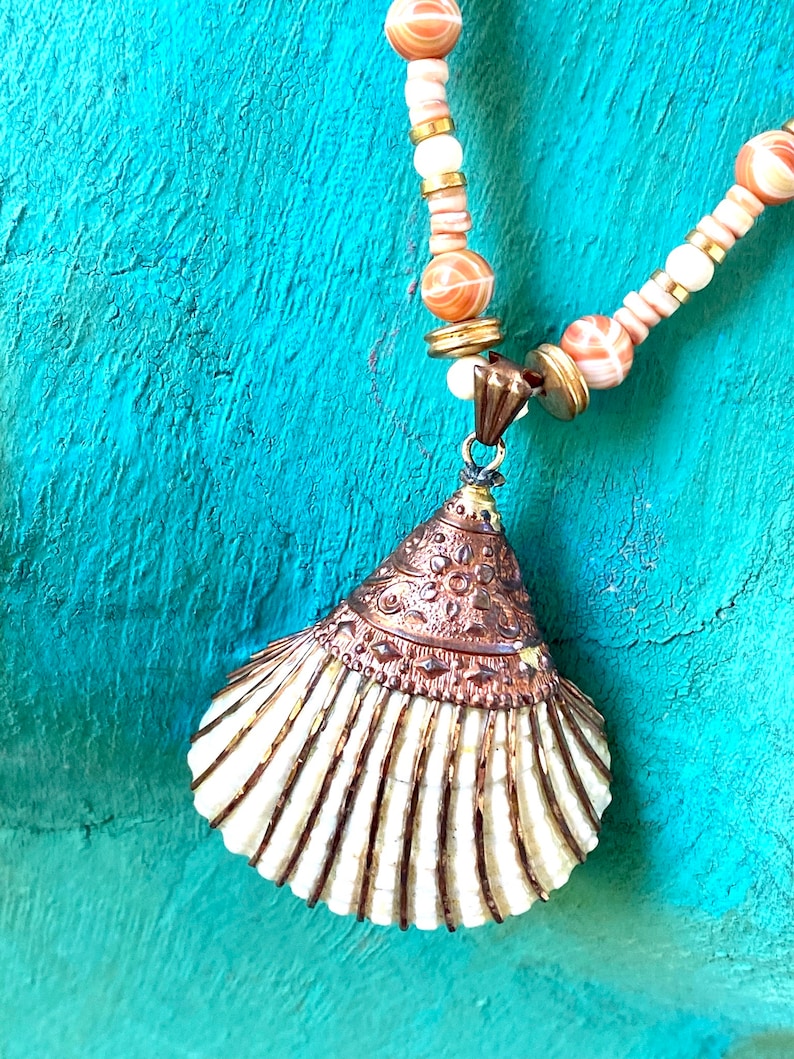 May include: A white seashell pendant necklace with a copper-toned top and a beaded chain with white and orange beads.