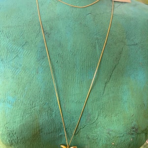 May include: A gold chain necklace with a gold pendant shaped like a stylized bird. The necklace is on a mannequin with a green background.