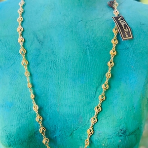 May include: A gold chain necklace with a delicate, openwork design. The chain is made of small, linked circles with a cutout pattern. The necklace is displayed on a turquoise mannequin.