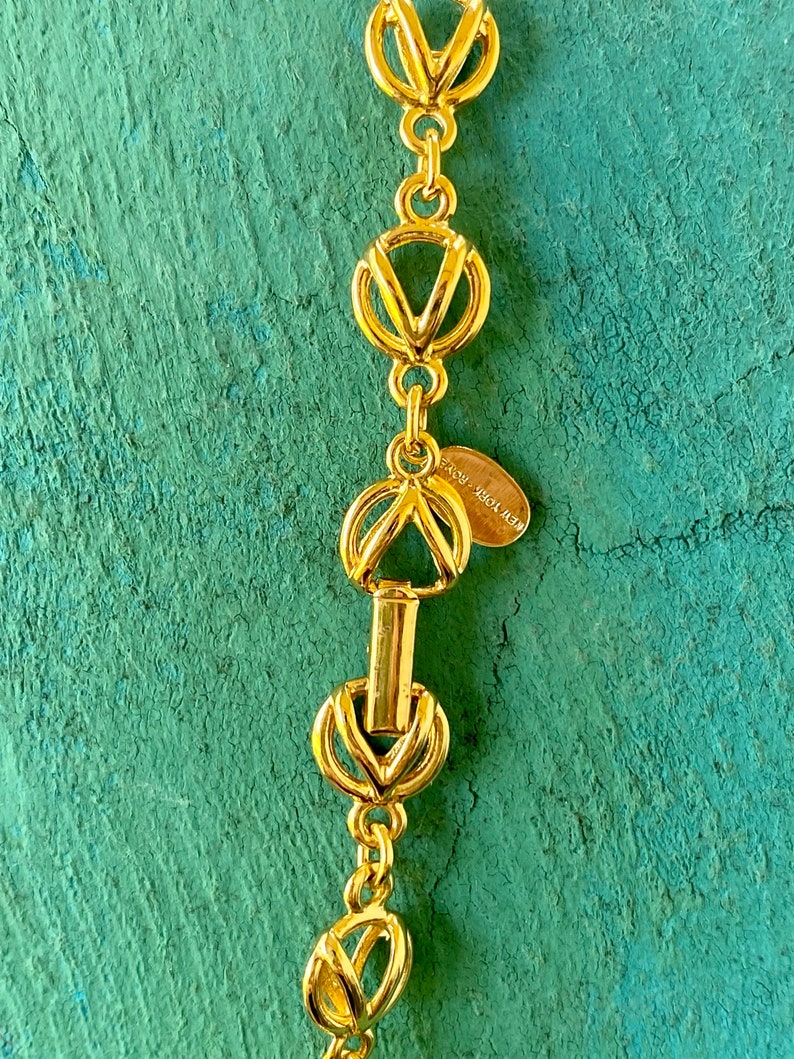 May include: Gold-toned necklace with a chain made of interlocking circles and V-shaped links. The necklace has a clasp with a small tag that reads "NEW YORK, NEW YORK".