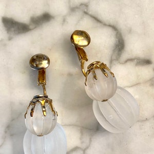 Puede incluir: Un par de pendientes de clip de tono dorado con colgantes de vidrio blanco esmerilado en forma de l&aacute;grima.