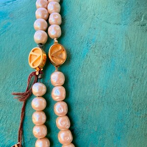 May include: A double strand pearl necklace with gold clasps. The clasps are round and have a letter 'V' design. The pearls are cream colored and have a slight iridescent sheen.