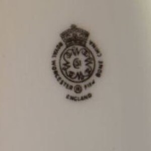 May include: A close-up of a white porcelain mark with a black crown, the words "Royal Crown Derby", "Worcester", "England", and the number "1154".