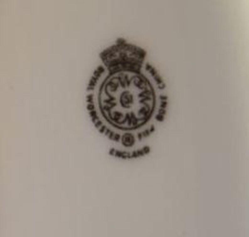 May include: A close-up of a white porcelain mark with a black crown, the words "Royal Crown Derby", "Worcester", "England", and the number "1154".