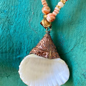 May include: A white seashell pendant necklace with a copper and gold-toned metal top. The necklace is made with white and orange striped beads and gold-toned beads.