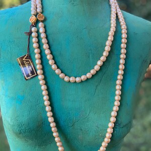 May include: A long, double-strand pearl necklace with gold clasps. The necklace is displayed on a mannequin with a teal-colored torso. The necklace has a tag that reads "Valentina".