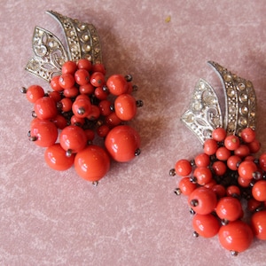 May include: A pair of dangle earrings with silver-toned metal settings and clusters of bright orange beads.