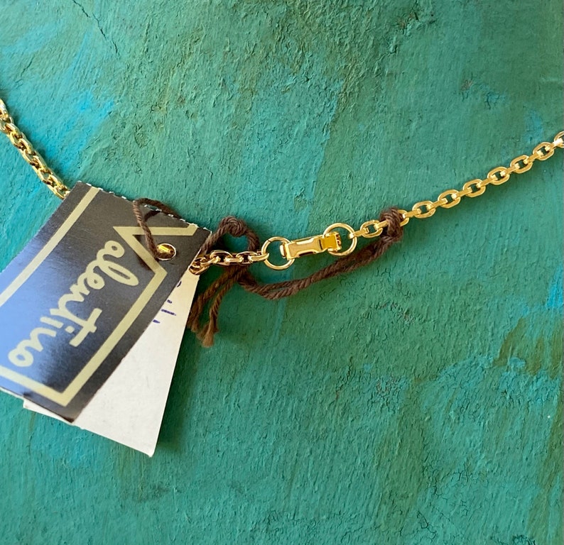 Puede incluir: Un collar de cadena dorada con una cuerda marr&oacute;n atada a un cierre. El collar tiene una etiqueta adjunta que dice "Glamour" en letras negras.