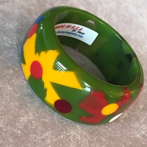 May include: Green, yellow, red, and white bangle bracelet with a floral design. The bracelet is made in the USA by Polo and is available at designbypolo.net.