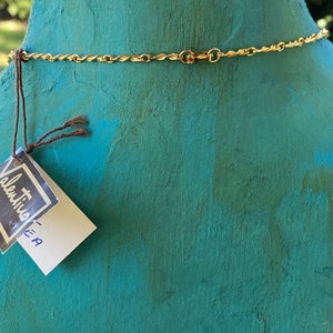 Puede incluir: Vista posterior de un collar de cadena dorada con cierre. El collar est&aacute; en un maniqu&iacute; turquesa. Una peque&ntilde;a etiqueta blanca con el texto "Valentino - EA" est&aacute; unida al maniqu&iacute;.