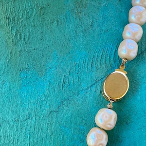 May include: A white pearl necklace with a gold clasp. The necklace is on a turquoise background.