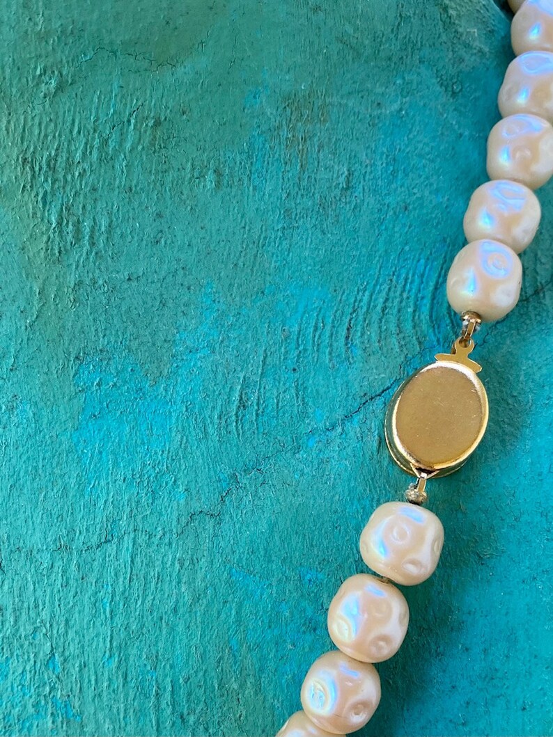 May include: A white pearl necklace with a gold clasp. The necklace is on a turquoise background.