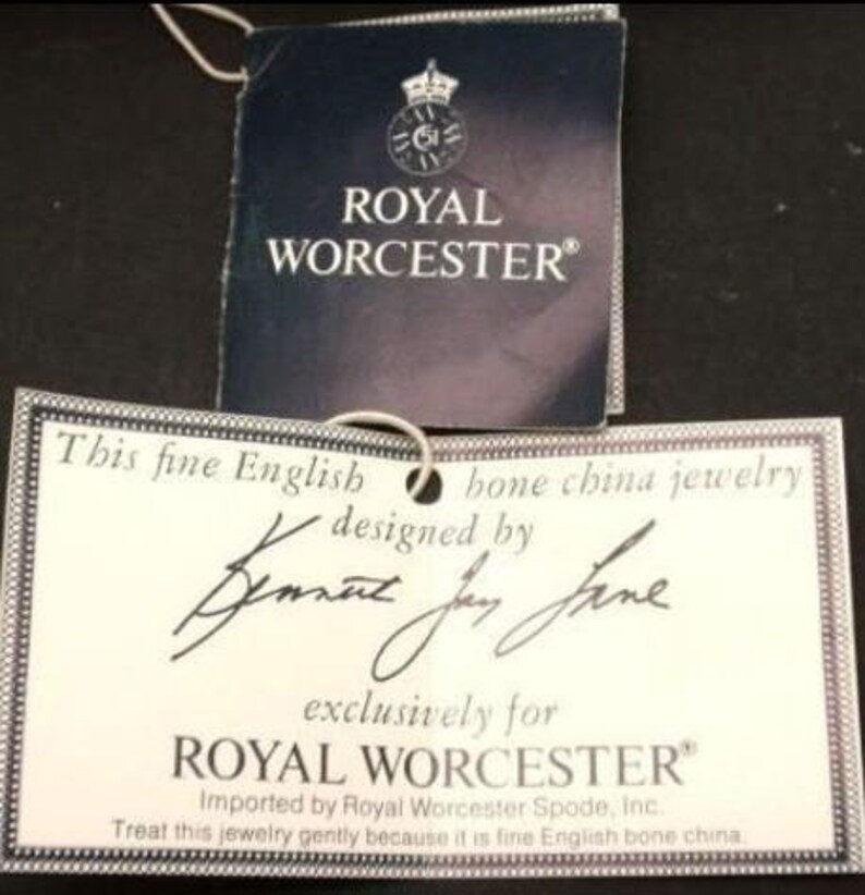 Peut inclure: Une &eacute;tiquette blanche avec du texte noir qui dit "This fine English bone china jewelry designed by  exclusively for ROYAL WORCESTER Imported by Royal Worcester Spode, Inc. Treat this jewelry gently because it is fine English bone china."
