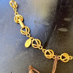 May include: A gold-toned necklace with a chain made of interlocking circles. The necklace has a small oval tag with the word "VALENTINO" inscribed on it.