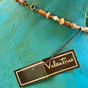 May include: A brown and white beaded necklace with a gold clasp and a brown tag that says "Valentino".