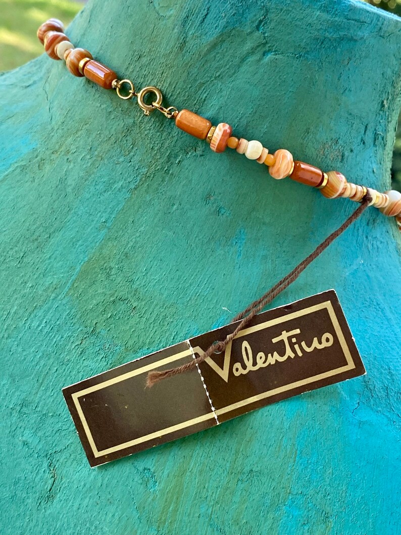 May include: A brown and white beaded necklace with a gold clasp and a brown tag that says "Valentino".