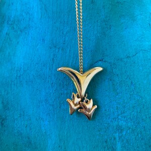 May include: A gold necklace with a pendant shaped like a bird with two smaller birds hanging from it.