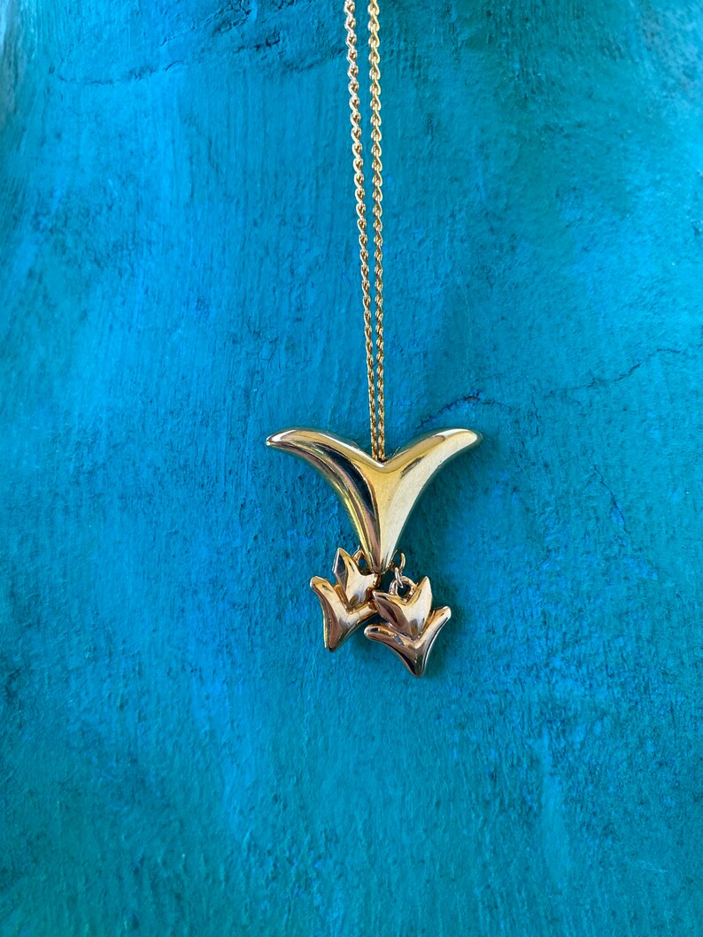 May include: A gold necklace with a pendant shaped like a bird with two smaller birds hanging from it.