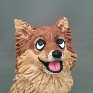 May include: A brown and tan ceramic figurine of a dog with a pink tongue sticking out. The dog has brown eyes and a black nose.