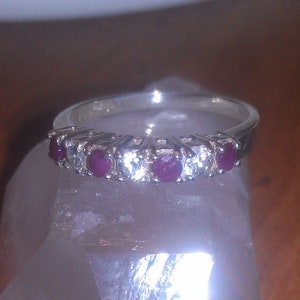 May include: A silver band ring with five red gemstones and five clear gemstones set in a prong setting.