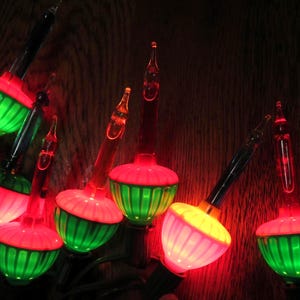 May include: A string of vintage-style Christmas bubble lights featuring glass bulbs with red, pink, or yellow tops and ribbed green bases. Each bulb contains a clear liquid tube that bubbles when heated, connected by a dark electrical cord.