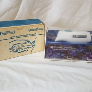 Könnte beinhalten: Weiße elektrische Schere in einem durchsichtigen Plastikkoffer mit einer blauen und weißen Schachtel. Die Schachtel trägt die Aufschrift "Penncrest Electric Scissors 2 Speeds with Light - Stainless Steel Blades".