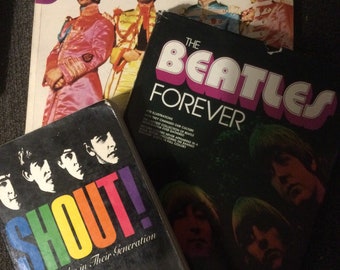 May include: Three vintage Beatles books. The first book is titled "The Beatles: An Illustrated Record" and features a rainbow design. The second book is titled "The Beatles Forever" and is black with pink lettering. The third book is titled "Shout! The Beatles in Their Generation" and is black with rainbow lettering.