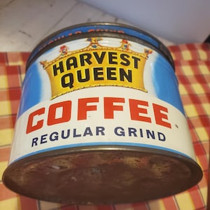 May include: Vintage Harvest Queen coffee tin. The tin is cylindrical with a blue and white background. The words "HARVEST QUEEN" are in black letters inside a yellow crown. The word "COFFEE" is in red letters, and "REGULAR GRIND" is below.