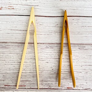 May include: Two pairs of wooden kitchen tongs. One pair is natural wood and the other is a darker brown wood.
