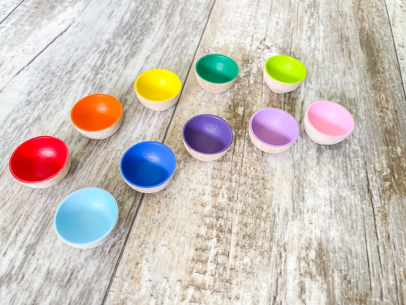 May include: A set of ten small wooden bowls in a rainbow of colors, arranged in a semi-circle on a light wood surface.