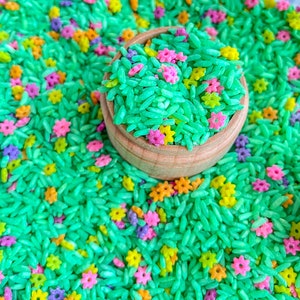 May include: A wooden bowl filled with green rice and colourful sprinkles. The sprinkles are shaped like flowers and stars.