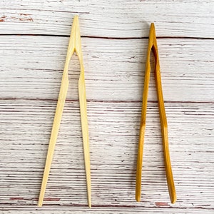 May include: Two pairs of wooden kitchen tongs. One pair is natural wood and the other is a darker brown wood.