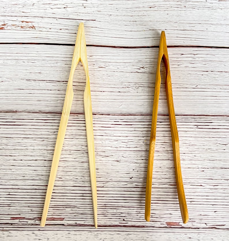 May include: Two pairs of wooden kitchen tongs. One pair is natural wood and the other is a darker brown wood.
