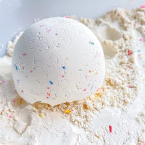 May include: A white cake mix ball with colorful sprinkles, partially submerged in a white powder, resembling a snow globe.